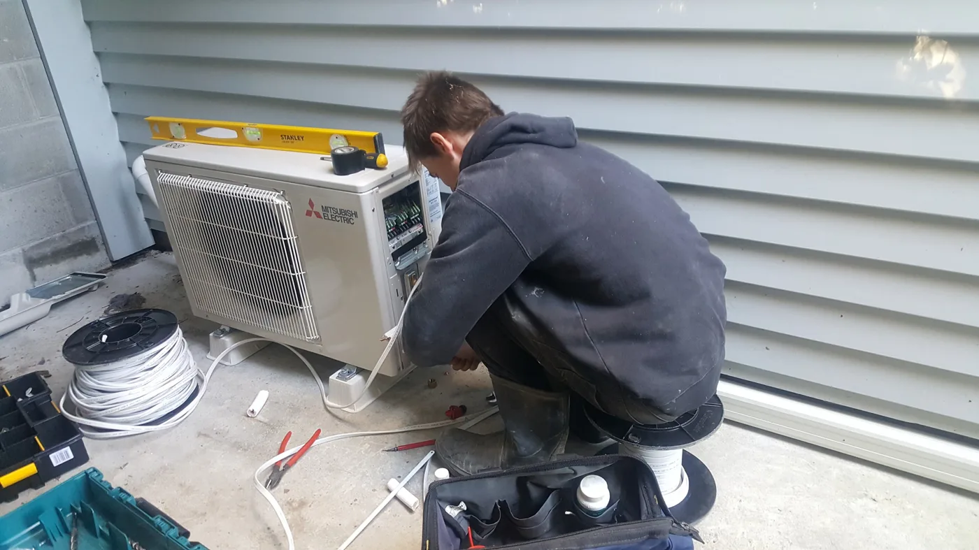 Technician working on an outdoor heat pump unit beside a house.